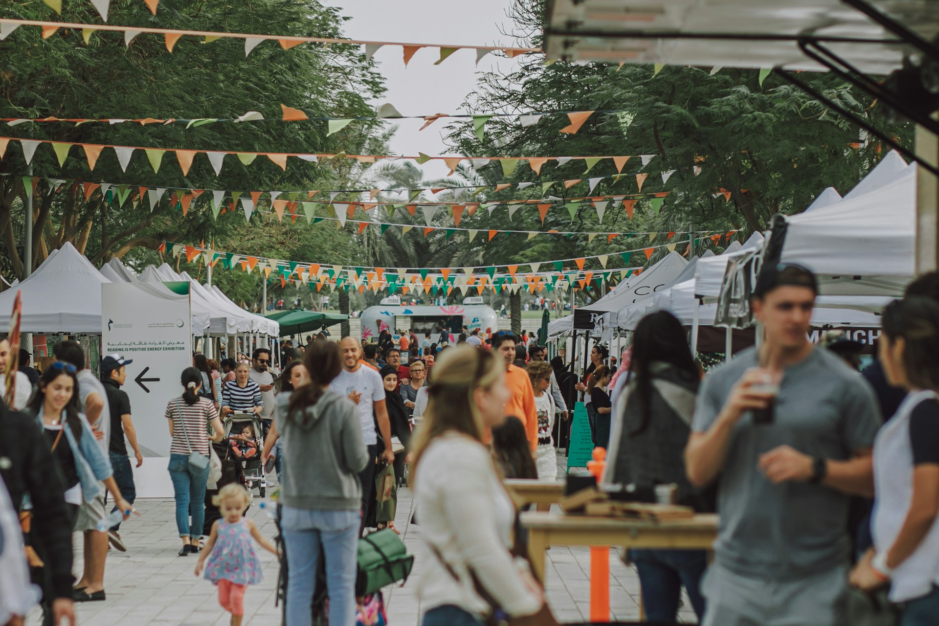 People walking through an open-air community market with outdoor vendor booths and local shoppers